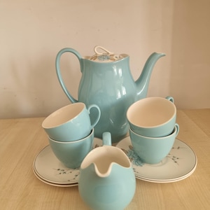 May include: A light blue vintage tea set comprising a teapot, creamer, saucers, and teacups. The teacups and creamer have a white interior. The saucers feature a floral pattern. The teapot has a curved handle and a lid.