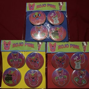 May include: Three sets of four round buttons featuring a cartoon pink and red furry creature with different expressions. The buttons are packaged on a colourful background with the text "ROJO PINK".
