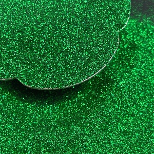 May include: Close-up of vibrant green glitter, scattered across a dark surface. The glitter is highly reflective, catching the light and creating a sparkling effect. The image shows a cloud-shaped object with a silver edge.
