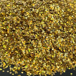 以下が含まれることがあります： 金色のグリッターの山をクローズアップ。グリッターの粒子は、メタリックな輝きを持つ小さな六角形の形をしています。グリッターは光を反射し、キラキラとした効果を生み出します。全体的な色は、他の色合いを持つ暖かい金色です。