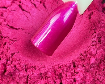 May include: A close-up of a vibrant magenta nail polish swatch on a white stick, set against a backdrop of matching magenta powder. The nail polish has a glossy, shimmering finish, reflecting light. The powder has a textured, granular appearance.
