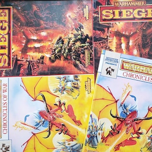 May include: Three Warhammer game books with colorful covers. The top book is titled "Warhammer Siege" and features a fantasy battle scene with orcs and humans. The middle book is titled "Warhammer Chronicles of War" and features a dragon and knights. The bottom book is titled "Warhammer Chronicles of War" and features a dragon and knights.