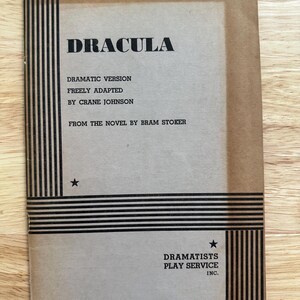Może przedstawiać: Beżowy scenariusz teatralny w miękkiej oprawie zatytułowany Dracula, będący dramatyczną wersją swobodnie zaadaptowaną przez Crane'a Johnsona na podstawie powieści Brama Stokera. Okładka zawiera czarne pionowe i poziome paski oraz dwie małe czarne gwiazdki.
