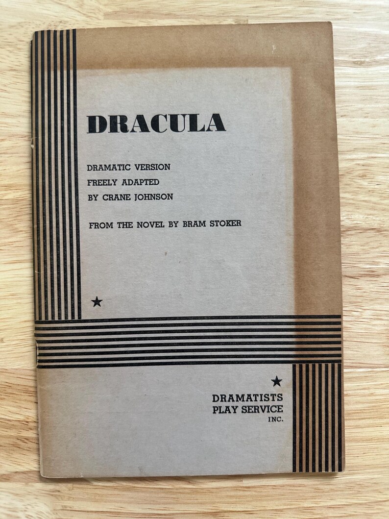 Może przedstawiać: Beżowy scenariusz teatralny w miękkiej oprawie zatytułowany Dracula, będący dramatyczną wersją swobodnie zaadaptowaną przez Crane'a Johnsona na podstawie powieści Brama Stokera. Okładka zawiera czarne pionowe i poziome paski oraz dwie małe czarne gwiazdki.