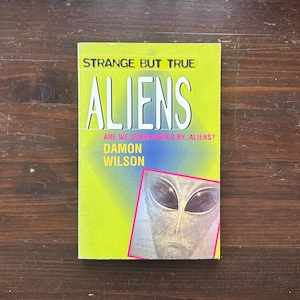 May include: A paperback book titled "Strange But True Aliens" with a neon green cover. The book features the title "ALIENS" in large white letters, the question "ARE WE SURROUNDED BY ALIENS?" and an illustration of an alien face.
