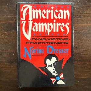 May include: A book titled "American Vampires: Fans, Victims, Practitioners" by Norine Dresser. The cover features a red background with a black and white illustration of a vampire with a red, white, and blue bow tie.