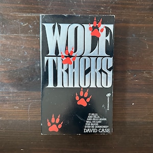 May include: A black paperback book with a silver title "WOLF TRACKS" and red paw prints. The text on the cover reads "IT KILLS AND KILLS. AND KILLS AGAIN WILL ITS LUST FOR BLOOD EVER BE QUENCHED? DAVID CASE"