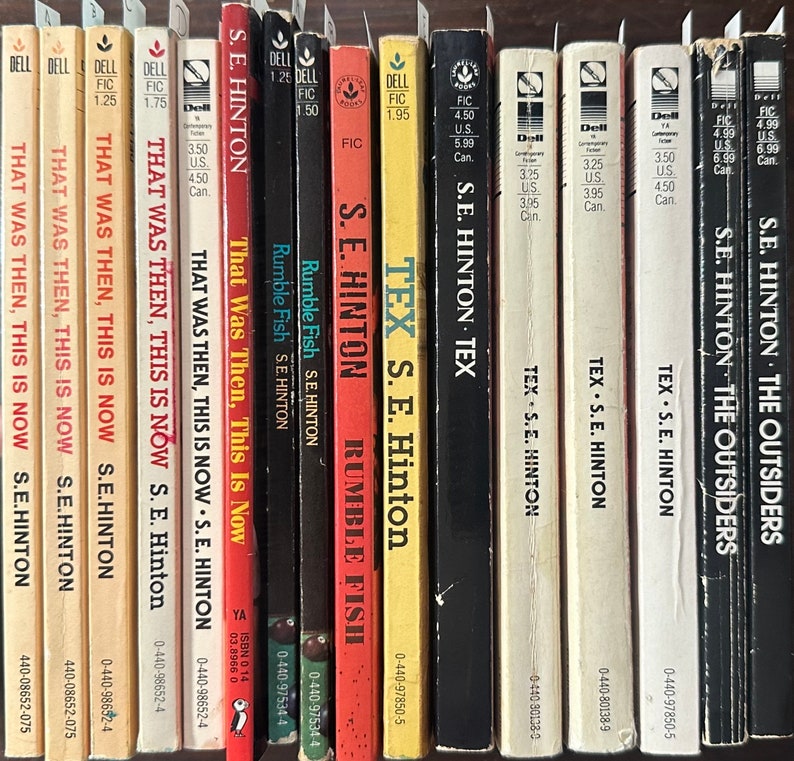 May include: A shelf of paperback books by S.E. Hinton, including titles like "That Was Then, This Is Now", "Rumble Fish", and "Tex".