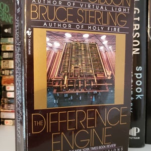 May include: A brown hardcover book with a gold title, "The Difference Engine" by William Gibson and Bruce Sterling. The cover features a futuristic cityscape with a large, intricate machine in the center. The book is part of the Spectra Special Editions series.