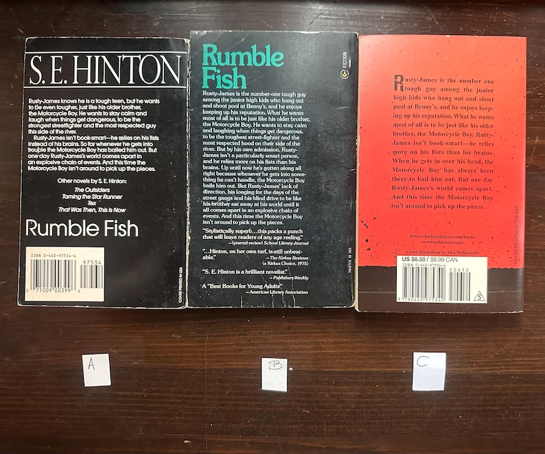 May include: Three paperback books with red, black, and white covers. The books are titled "Rumble Fish" by S.E. Hinton. The back covers feature text about the books and the author.