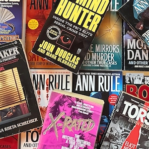May include: A collection of paperback true crime novels with various titles and authors. The books are stacked and arranged in a random order. Some of the titles include "The Shoemaker", "Mind Hunter", "The Most Wanted Killer", and "The Fall of the Godfather: Ross".