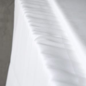 Puede incluir: Primer plano de tela blanca con pliegues y sombras suaves. La tela parece estar drapeada, con una textura sutil y una apariencia brillante y limpia. La imagen tiene una est&eacute;tica minimalista.