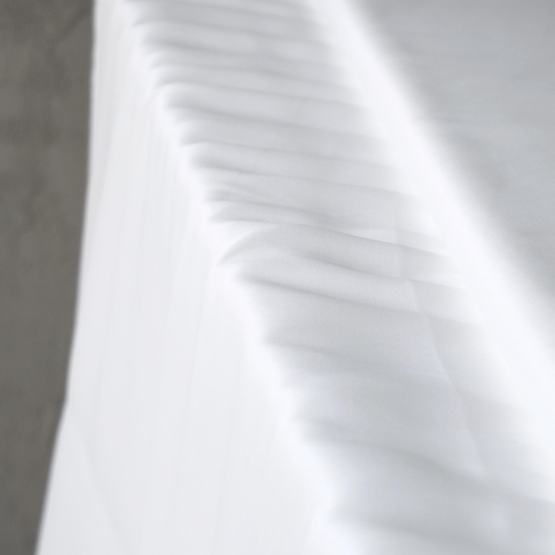 Puede incluir: Primer plano de tela blanca con pliegues y sombras suaves. La tela parece estar drapeada, con una textura sutil y una apariencia brillante y limpia. La imagen tiene una est&eacute;tica minimalista.