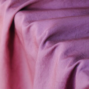 Pode incluir: Close-up de um tecido drapeado em tons de roxo e rosa. O tecido tem uma apar&ecirc;ncia texturizada com linhas diagonais vis&iacute;veis, criando uma sensa&ccedil;&atilde;o de profundidade e movimento. As dobras e as sombras adicionam interesse visual.