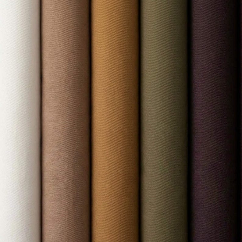 K&ouml;nnte beinhalten: F&uuml;nf vertikale Stoffrollen, die nebeneinander angeordnet sind und eine K&ouml;perbindung aufweisen. Die Farben von links nach rechts sind Cremewei&szlig;, Hellbraun, Goldbraun, Olivgr&uuml;n und Dunkellila, was einen Verlauf neutraler Farbt&ouml;ne ergibt.