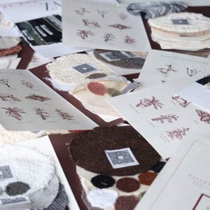 Puede incluir: Una colección de muestras de tela y tarjetas informativas con ilustraciones botánicas y códigos QR. Las muestras incluyen varias texturas y colores como blanco, marrón y gris. Las tarjetas muestran texto impreso y diagramas.