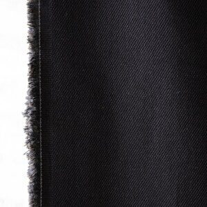 Puede incluir: Primer plano de tela vaquera negra con un borde deshilachado en el lado izquierdo. La tela tiene un patr&oacute;n de tejido diagonal y un color oscuro y s&oacute;lido. La textura parece suave y ligeramente texturizada, adecuada para ropa.