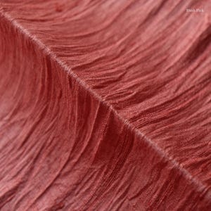 May include: Close-up of a textured fabric in a blush pink hue. The fabric has a crinkled, wavy pattern, with visible folds and ridges. The words "Blush Pink" are visible in the upper right corner.