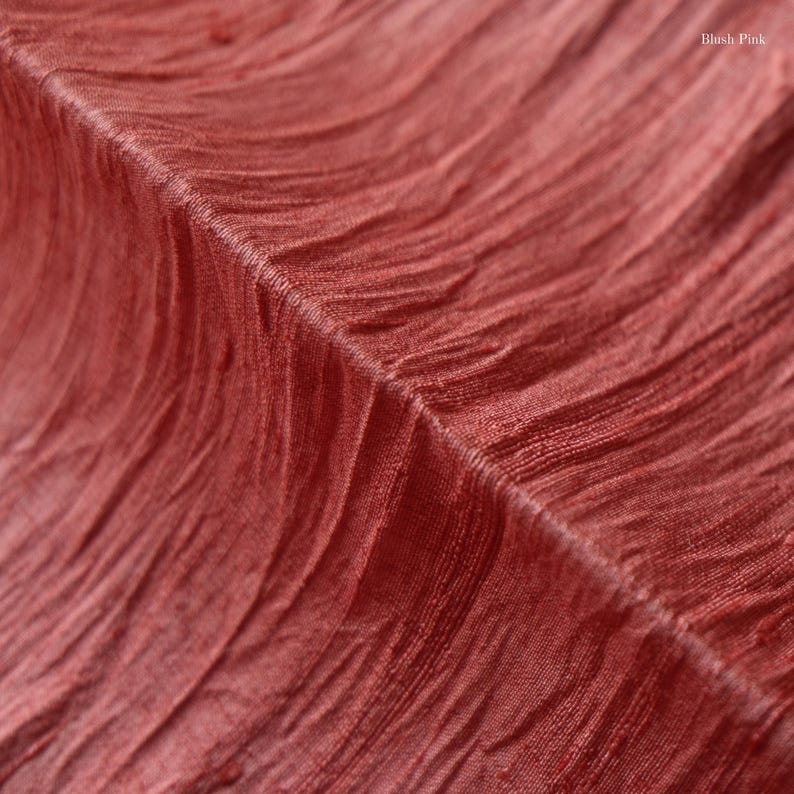 May include: Close-up of a textured fabric in a blush pink hue. The fabric has a crinkled, wavy pattern, with visible folds and ridges. The words "Blush Pink" are visible in the upper right corner.