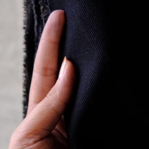 Puede incluir: Primer plano de una tela azul marino oscuro con un tejido texturizado. La tela se sostiene, mostrando la textura y el color. El borde de la tela es visible en el lado izquierdo.