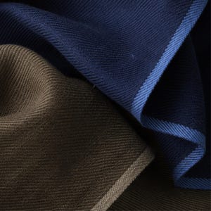 May include: A close-up view of two folded pieces of fabric. One piece is a deep navy blue with a lighter blue stitched border, and the other piece is a solid brown with a tan stitched border. Both fabrics feature a fine, uniform knit texture.