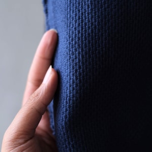 Puede incluir: Una tela de color azul marino profundo que presenta una textura de tejido de cesta densa y distintiva. El material muestra un patrón de cuadrícula consistente y repetitivo de hilos entrelazados, creando una superficie táctil con profundidad visible y un color azul oscuro uniforme.