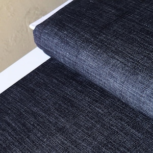 May include: Close-up of dark blue denim fabric with a subtle texture. The fabric is folded over, showing the weave of the material.
