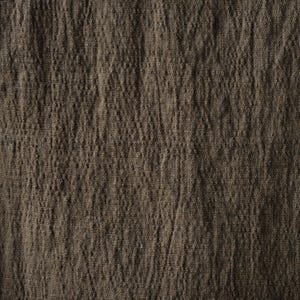 May include: Close-up of a textured, brown fabric. The fabric has a slightly wrinkled appearance, with vertical lines and subtle variations in color. The material appears to be a natural fiber, possibly linen or cotton, with a rustic aesthetic.