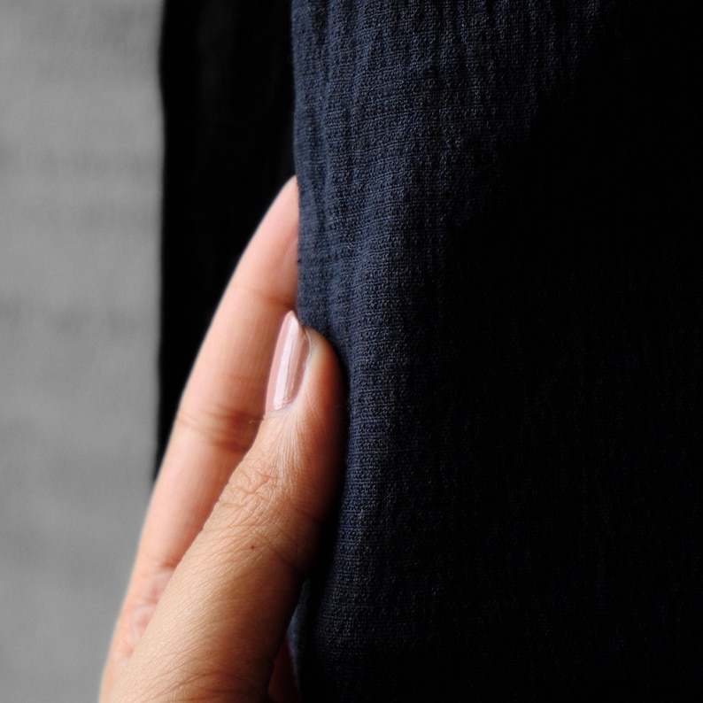 May include: Close-up of a hand holding a piece of dark blue fabric. The fabric has a textured appearance. The person's fingernails are painted with a light pink polish.