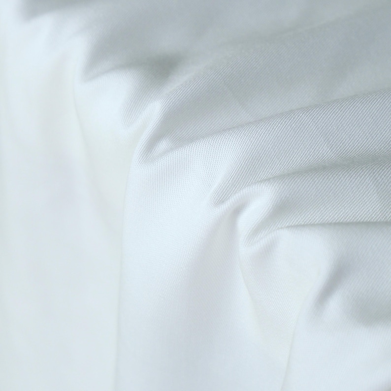 Pode incluir: Close-up de tecido branco com textura e dobras vis&iacute;veis. O tecido parece ser um material liso e tecido, possivelmente algod&atilde;o ou um t&ecirc;xtil semelhante. A ilumina&ccedil;&atilde;o cria sombras que enfatizam a textura e a profundidade do tecido.