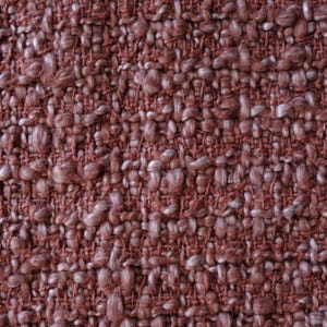 May include: Close-up of a textured fabric with a woven pattern. The fabric is primarily a muted reddish-brown color, with lighter, off-white fibers interspersed throughout. The weave creates a slightly bumpy, tactile surface.