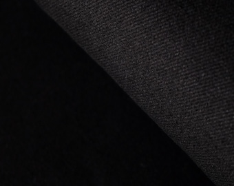 May include: Close-up of a black fabric with a textured surface. The fabric is folded over, revealing a darker, shadowed area. The material appears to be a heavy weave, possibly denim or a similar textile.