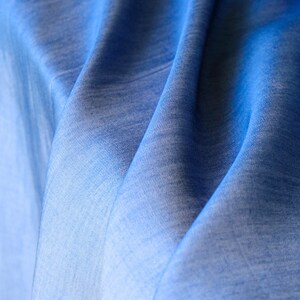 May include: Close-up of a flowing blue fabric. The material has a soft texture with subtle colour variations, creating a gradient effect. The folds and curves of the fabric are visible, suggesting a lightweight material.