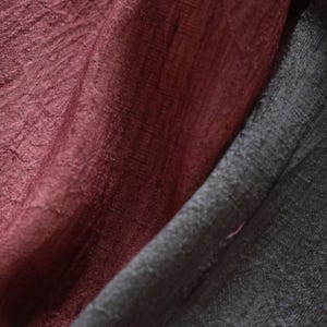 May include: Close-up of draped fabric in shades of burgundy and charcoal gray. The burgundy fabric has a textured, crinkled appearance, while the gray fabric appears smooth. The folds and shadows create depth and visual interest. Ideal for textile and fabric products.