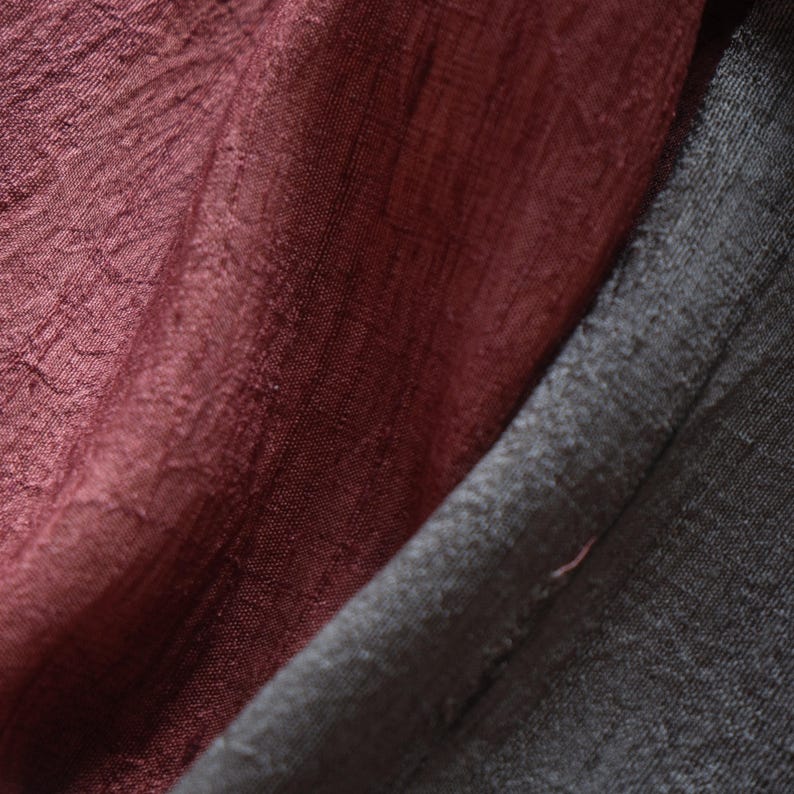 May include: Close-up of draped fabric in shades of burgundy and charcoal gray. The burgundy fabric has a textured, crinkled appearance, while the gray fabric appears smooth. The folds and shadows create depth and visual interest. Ideal for textile and fabric products.