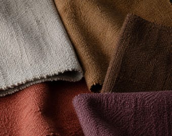 May include: A collection of five fabric swatches featuring a textured, woven surface. The colors include light beige, golden tan, dark brown, terracotta orange, and deep plum. Each piece of fabric is folded to display the weave and texture.