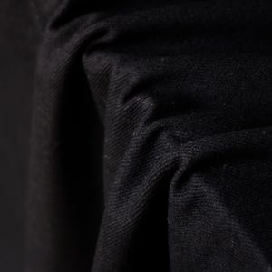 Puede incluir: Primer plano de tela negra con textura y pliegues visibles. El material parece grueso y opaco, con un acabado mate. La imagen resalta la profundidad y la dimensi&oacute;n del textil.