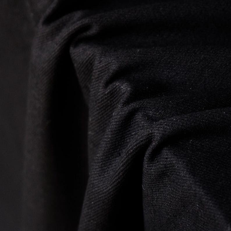 Puede incluir: Primer plano de tela negra con textura y pliegues visibles. El material parece grueso y opaco, con un acabado mate. La imagen resalta la profundidad y la dimensi&oacute;n del textil.