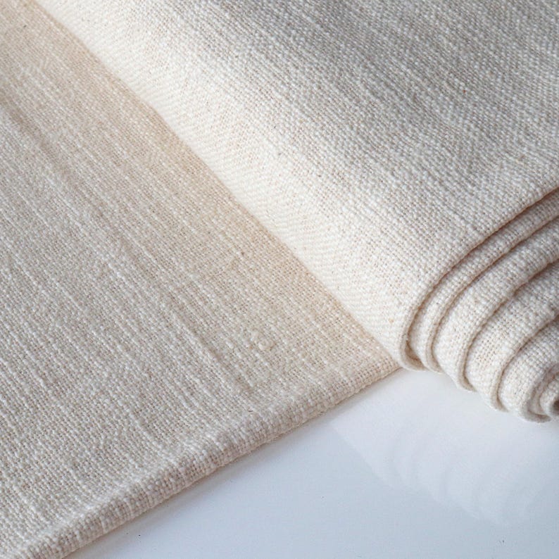 May include: A close-up of a folded piece of off-white fabric with a textured weave. The fabric is soft and has a natural look.