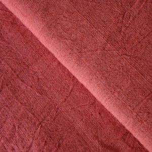 Könnte beinhalten: Nahaufnahme eines gefalteten, korallenfarbenen Stoffstücks. Der Stoff hat eine strukturierte Oberfläche mit sichtbarem Gewebe und subtilen Farbtonvariationen. Die Falten erzeugen Schatten, die dem Bild Tiefe verleihen. Das Material scheint weich zu sein, möglicherweise Leinen oder Baumwolle.