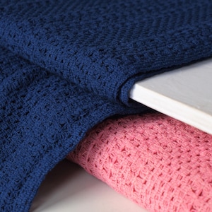 May include: Close-up of two folded textiles. One is a deep navy blue, the other is a soft pink. Both textiles have a textured, open weave pattern. The fabrics are draped over a white surface, creating a layered effect.