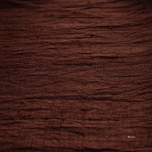 May include: Close-up of a textured fabric in a rich mocha brown color. The fabric has a slightly wrinkled appearance, with horizontal lines and subtle variations in tone. The word "Mocha" is visible in the bottom right corner.