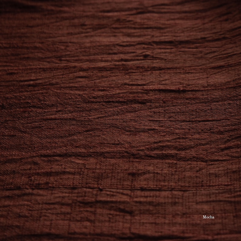 May include: Close-up of a textured fabric in a rich mocha brown color. The fabric has a slightly wrinkled appearance, with horizontal lines and subtle variations in tone. The word "Mocha" is visible in the bottom right corner.