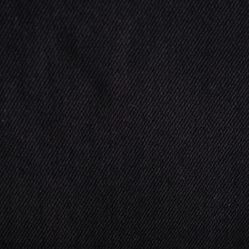 Puede incluir: Primer plano de tela vaquera negra. La tela presenta un patr&oacute;n de tejido diagonal, creando una superficie texturizada. El color es negro s&oacute;lido y profundo, con sutiles variaciones de tono debido al tejido.