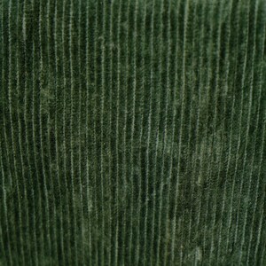May include: Close-up of a textured, dark green corduroy fabric. The fabric has vertical ridges, creating a ribbed pattern. The color is a deep, muted green, with subtle variations in tone across the surface.
