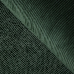 May include: Close-up of a dark green corduroy fabric. The fabric has a ribbed texture with vertical lines. The material is folded over, revealing the texture and color variations. The fabric appears soft and plush.