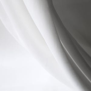 Puede incluir: Primer plano de tela blanca con pliegues suaves y sombras. La tela parece ligera, posiblemente lino o similar, con una textura sutil. La iluminaci&oacute;n crea un efecto de gradiente, pasando de blanco brillante a un gris m&aacute;s oscuro.