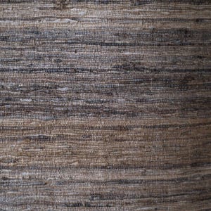 May include: A woven fabric with a horizontal striped pattern featuring a blend of earthy tones including dark brown, light tan, beige, and charcoal grey. The texture is coarse and uneven, with visible thick and thin threads interlaced throughout.