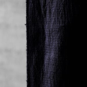 May include: Close-up of a dark blue fabric with a textured weave. The fabric appears to be a heavy linen or similar material, with a slightly frayed edge. The background is a light gray, providing contrast.