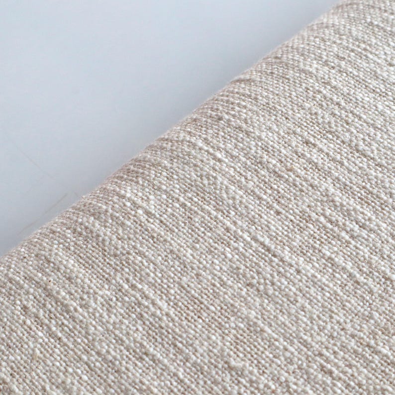May include: Close-up of a beige fabric with a textured weave. The fabric has a subtle sheen and a slightly rough feel.
